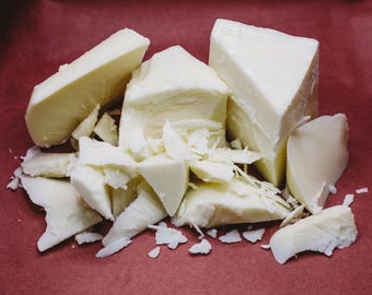 May include: A close-up of white cheese broken into pieces on a red surface. The cheese is in various shapes and sizes, some are large chunks and others are small, thin pieces.
