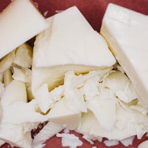 May include: Several irregular chunks of off-white, solid wax or soap material. The pieces vary in size, ranging from large, smooth-surfaced triangular wedges to smaller, jagged, and flaky fragments scattered throughout the center of the composition.