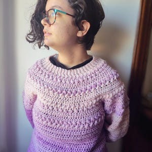 May include: A purple and pink ombre crochet sweater with a textured stitch pattern.
