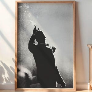 May include: A rectangular framed wall art print featuring a black and white silhouette of a person in a suit standing with one arm raised, set against a bright, hazy background. The artwork is displayed in a light-toned wooden frame.