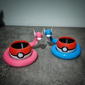 Può includere: Due fioriere a tema Pokémon stampate in 3D. Una è rosa con una Poké Ball rossa e bianca, l'altra è blu con una Poké Ball rossa e bianca. Ogni fioriera ha un interno nero e una testa a forma di drago.