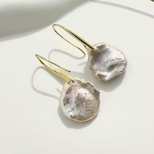 May include: A pair of gold dangle earrings with large, irregular shaped, iridescent pink pearls.