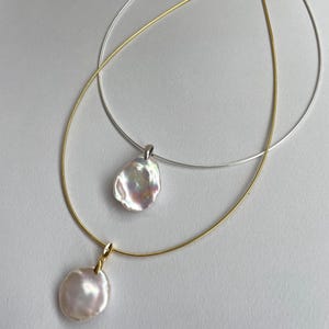 May include: Two necklaces with pearl pendants. The top necklace is silver and the bottom necklace is gold. Both necklaces have a single pearl pendant.
