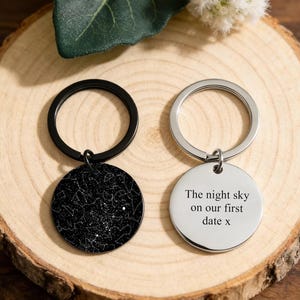 May include: Two keyrings with circular pendants. One pendant is black with a white star map design. The other is silver with the text "The night sky on our first date x". Both have metal key rings.