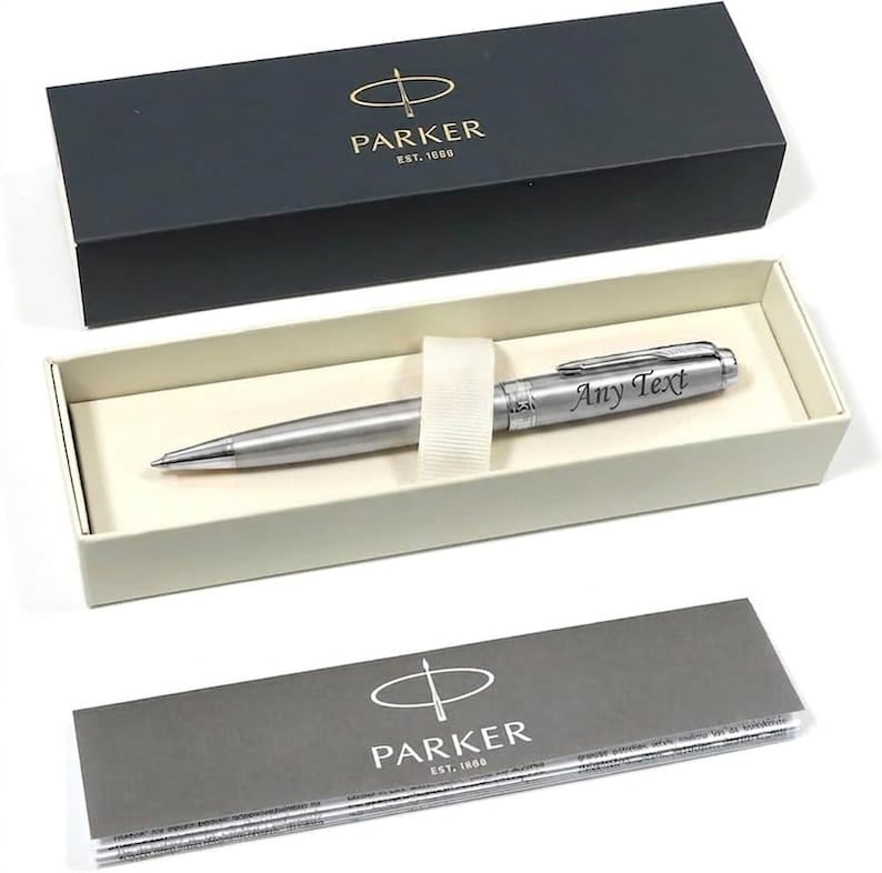 May include: A silver Parker pen with the text "Any Text" engraved on the barrel, presented in a black box with the Parker logo. The pen rests in a cream-colored interior, accompanied by a gray information card.