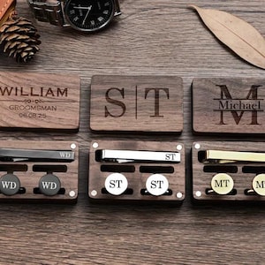 May include: Six wooden boxes with engraved initials and names. Each box contains a tie clip and cufflinks. The boxes are arranged in two rows of three. The top row has the names William, ST, and Michael. The bottom row has the initials WD, ST, and MT.