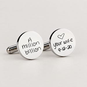May include: A pair of round, polished silver-tone metal cufflinks. One cufflink is engraved with the text 'A million billion' and the other features a hand-drawn heart, the text 'your wife', and the date '9-12-20' in a black script font.