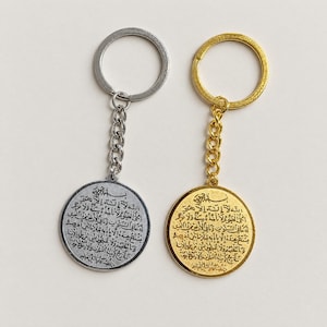 May include: Two circular keychains, one silver-toned and one gold-toned, each featuring a metal ring and a short chain. Both pendants are engraved with intricate Arabic calligraphy text covering the entire surface of the round metal discs.