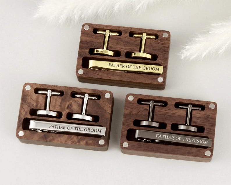 May include: Three wooden boxes with engraved metal cufflinks and tie bars. Each box has a different inscription: "Father of the Groom".