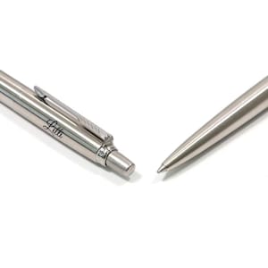 K&ouml;nnte beinhalten: Ein silberfarbener Kugelschreiber aus Metall mit Taschenclip und Druckknopfmechanismus. Der Schaft des Stiftes ist mit dem Namen Lilli in einer Schreibschrift graviert. Der Stift ist in zwei separaten Teilen dargestellt, dem Oberteil und der Spitze.
