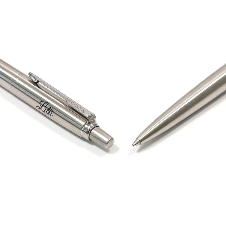 K&ouml;nnte beinhalten: Ein silberfarbener Kugelschreiber aus Metall mit Taschenclip und Druckknopfmechanismus. Der Schaft des Stiftes ist mit dem Namen Lilli in einer Schreibschrift graviert. Der Stift ist in zwei separaten Teilen dargestellt, dem Oberteil und der Spitze.