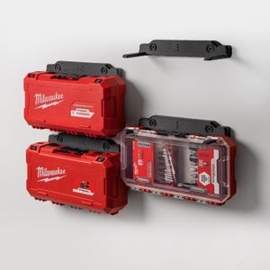 Puede incluir: Cajas de herramientas rojas Milwaukee y una funda transparente con herramientas montadas en una pared blanca. Las cajas de herramientas tienen soportes de montaje negros. El logotipo de Milwaukee es visible en las cajas de herramientas. La funda transparente contiene varias herramientas.