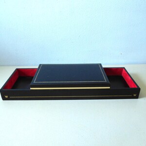 May include: A rectangular black tray with a vibrant red interior lining and a matching black lid. The exterior features gold-colored decorative trim along the edges and a small gold crown emblem on the front side of the tray base.