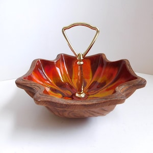 May include: A vintage serving dish with a unique leaf-like shape. The interior features a vibrant blend of orange, yellow, and red hues, complemented by a gold-toned handle. The exterior has a textured, wood-like appearance, adding to its retro charm.