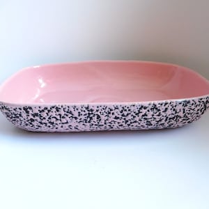 May include: A pink ceramic serving dish with a black speckled design. The dish is rectangular and has a slightly rounded edge.