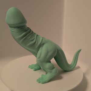 Könnte beinhalten: Eine grüne 3D-gedruckte Dinosaurierfigur mit einem langen Schwanz und einer einzigartigen Kopfform.