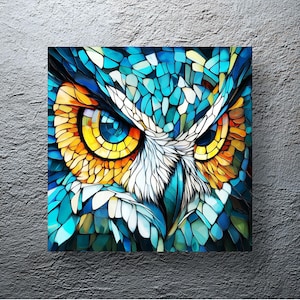 Op de afbeelding: Vierkant canvas kunstwerk met een mozaïekstijl uilenportret. Het gezicht van de uil is weergegeven in tinten blauw, turquoise, geel en wit, wat een opvallend visueel effect creëert. Het kunstwerk is gemonteerd op een getextureerde grijze muur.