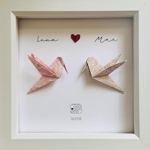 May include: A white framed artwork with two origami birds, one pink and one beige. The names "Luna" and "Max" are above the birds, with a red heart between them. The date "060318" is displayed below the birds.