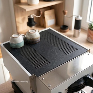 Peut inclure: Une machine à expresso blanche dotée d'un plateau chauffe-tasses noir texturé avec des fentes de ventilation intégrées. Deux petites tasses en céramique à glaçure mouchetée sont posées dessus. L'appareil possède une façade en inox et une poignée noire.