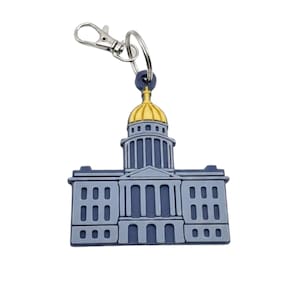 May include: A blue and gray keychain featuring a detailed depiction of a capitol building with a gold dome. The keychain has a silver clasp and a split ring for attaching keys. The building design is a two-tone color scheme.