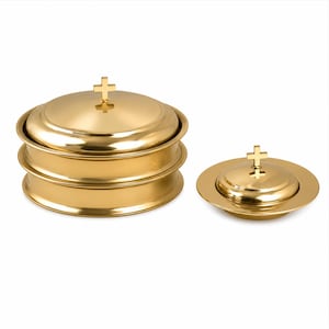 Può includere: Un set di vasi liturgici in metallo color oro lucido, composto da una pila di tre contenitori circolari con coperchio e una ciotola più piccola abbinata con coperchio. Ogni coperchio è sormontato da una piccola croce dorata verticale.