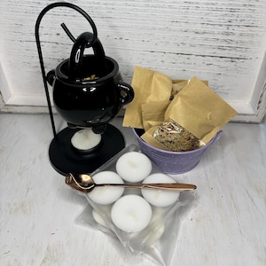 Puede incluir: Quemador de incienso de caldero negro con un soporte de metal, una cuchara pequeña y un paquete de incienso. El caldero está lleno de incienso suelto y hay velas de té delante de él. También hay un pequeño cubo morado con un paquete de incienso suelto dentro.