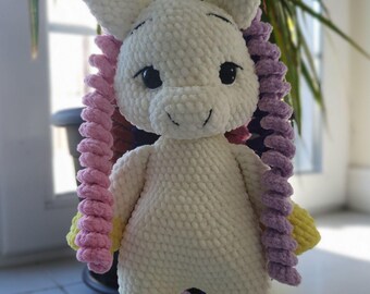 May include: A handmade white plush unicorn with a yellow horn, yellow hooves, and pink and purple curly hair. The unicorn has black eyes and a smiling expression. The plush toy is standing upright.