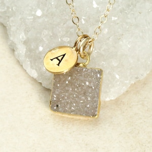 May include: Gold necklace with a square shaped white agate pendant and a small gold charm with the letter A.