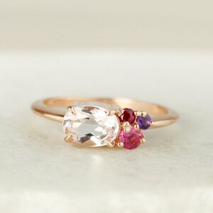 May include: A rose gold ring with a large oval-shaped clear gemstone and smaller pink, red, and purple gemstones.