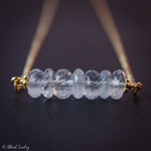 May include: A delicate gold chain necklace with a row of clear aquamarine gemstones.
