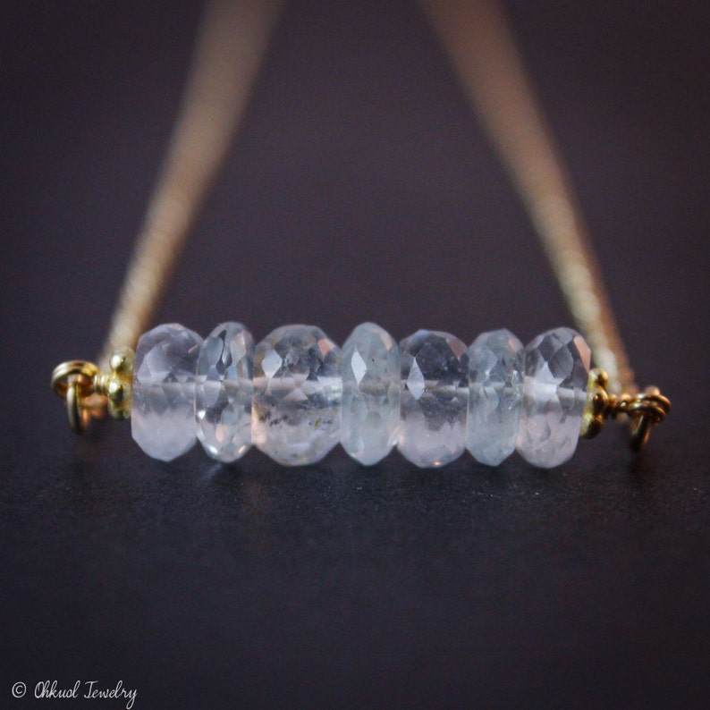 May include: A delicate gold chain necklace with a row of clear aquamarine gemstones.
