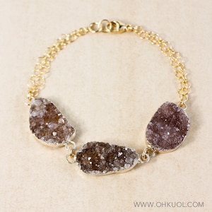 May include: A gold chain bracelet with three large, irregular shaped, light brown and purple crystal stones.