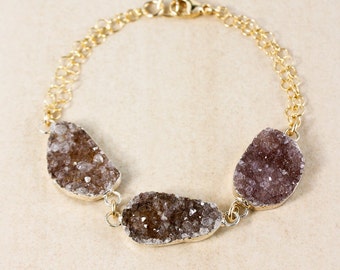 May include: A gold chain bracelet with three large, irregularly shaped, light brown and purple crystal stones.