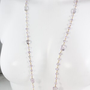 May include: A long, delicate necklace made of small, faceted amethyst beads and gold chain. The necklace is displayed on a white mannequin.
