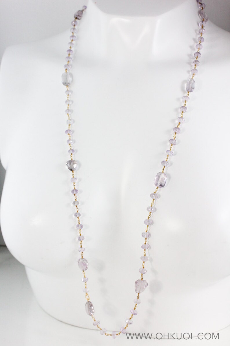 May include: A long, delicate necklace made of small, faceted amethyst beads and gold chain. The necklace is displayed on a white mannequin.