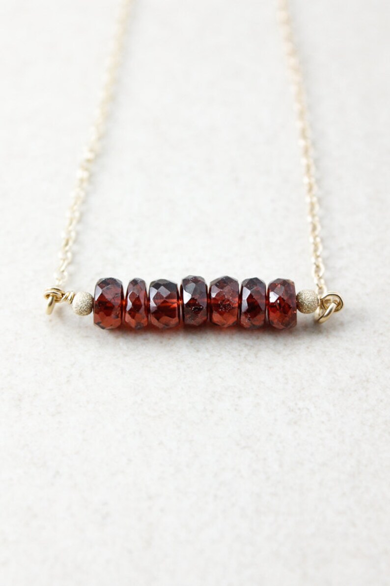 Pu&ograve; includere: Una collana con catena d'oro con una barra di perle di granato sfaccettate.