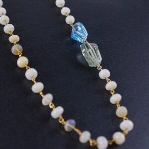 May include: A gold chain necklace with white opal beads and two faceted gemstone pendants, one blue and one green.