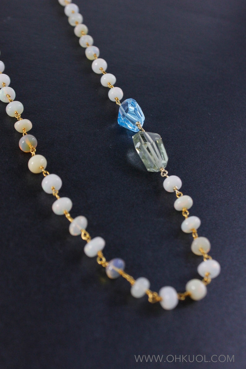 May include: A gold chain necklace with white opal beads and two faceted gemstone pendants, one blue and one green.