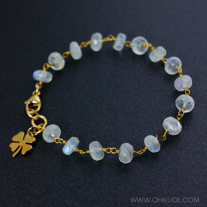 May include: A gold chain bracelet with a four-leaf clover charm and white moonstone beads.