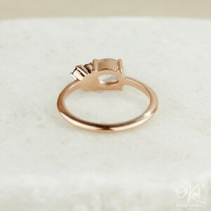 May include: A rose gold ring with a clear oval-shaped gemstone and a smaller, purple gemstone on the side.