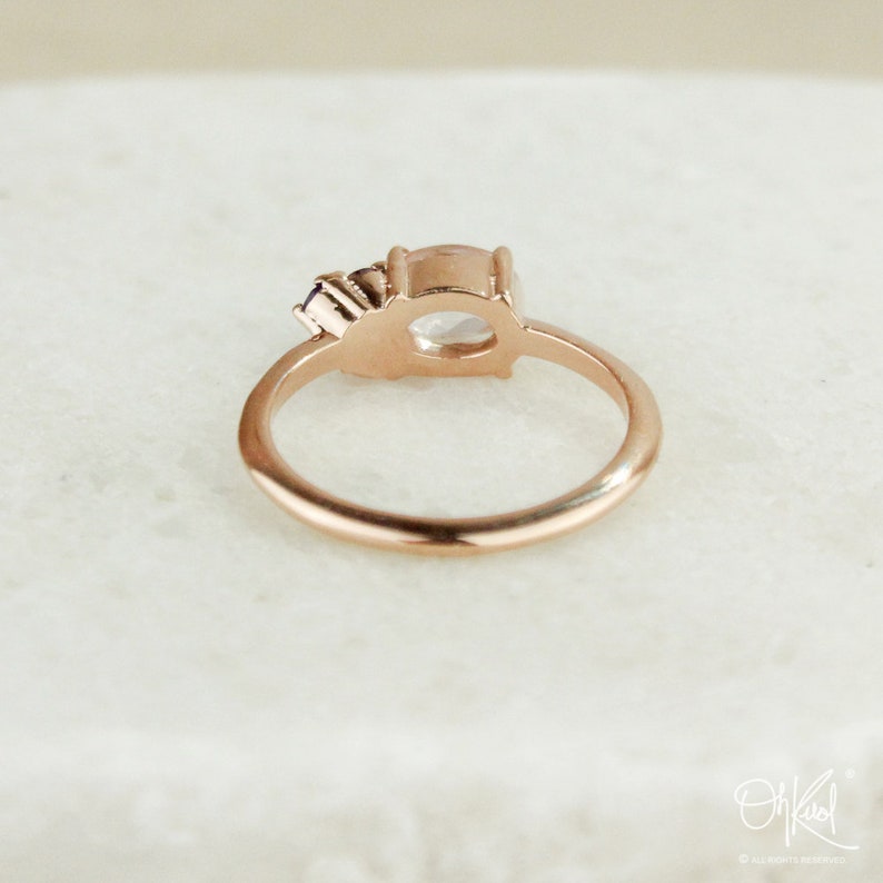 May include: A rose gold ring with a clear oval-shaped gemstone and a smaller, purple gemstone on the side.