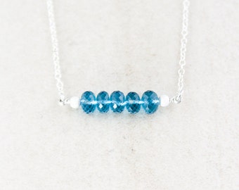 May include: A silver chain necklace with a row of blue topaz gemstones.