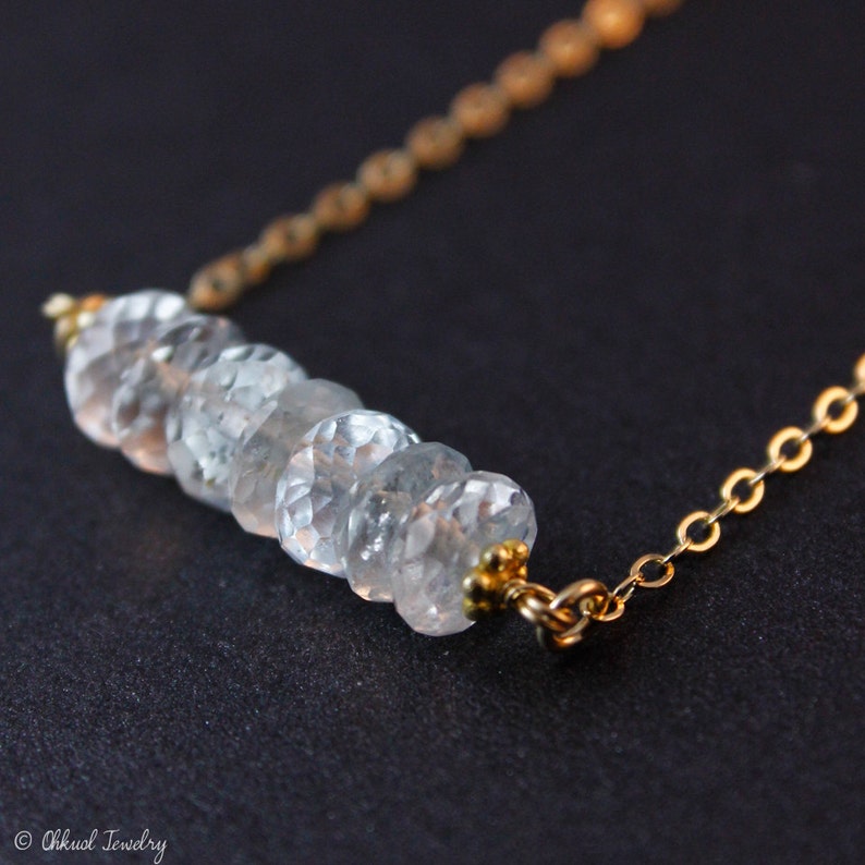 May include: A delicate gold chain necklace with a row of clear faceted gemstone beads.