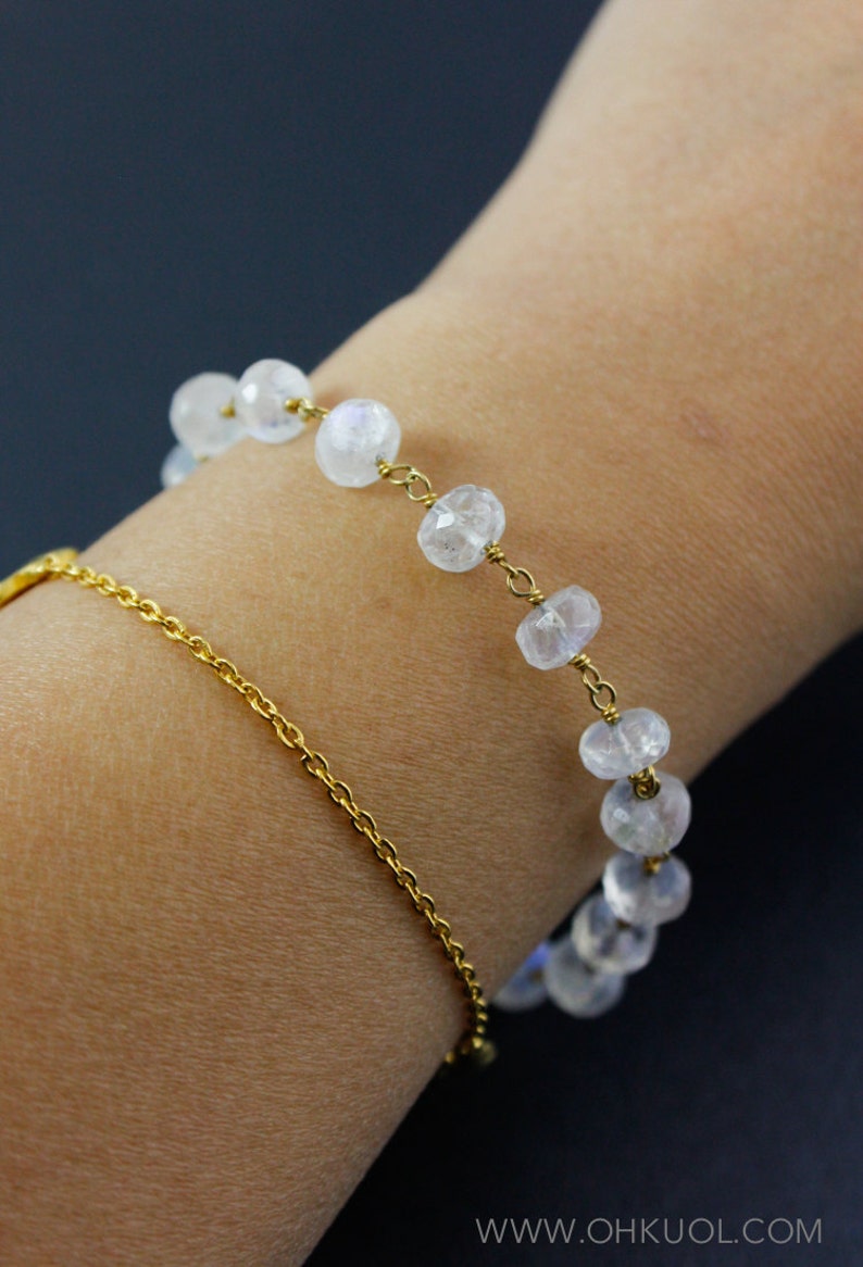 May include: A gold chain bracelet with a row of clear, faceted gemstone beads. The bracelet is worn on a person's wrist.