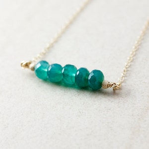 May include: A delicate gold chain necklace with a row of six teal green gemstone beads.