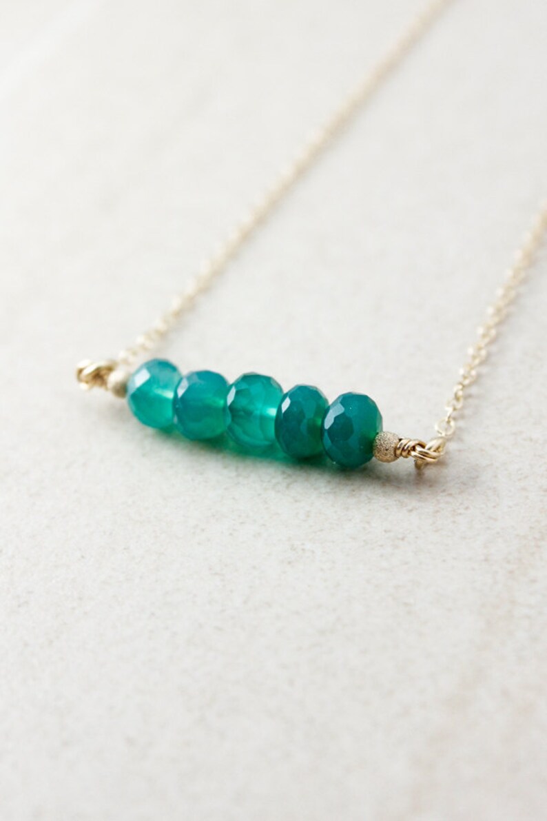 May include: A delicate gold chain necklace with a row of six teal green gemstone beads.