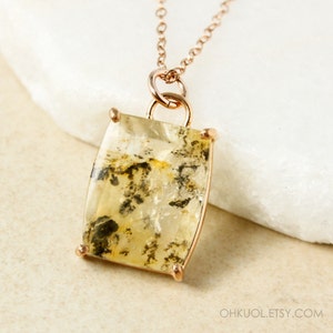 May include: A rose gold necklace with a large, rectangular, clear quartz pendant with black and brown inclusions. The pendant is set in a rose gold bezel setting.