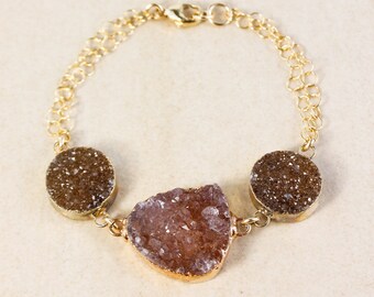 May include: A gold chain bracelet with three brown and pink agate crystal charms. The charms are in the shape of a circle and a freeform shape.
