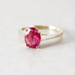 Può includere: Un anello d'oro con una grande pietra preziosa rosa di forma ovale incastonata a griffe.