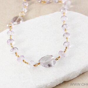 May include: A delicate gold chain necklace with light purple faceted beads and a larger, faceted, light purple gemstone pendant.